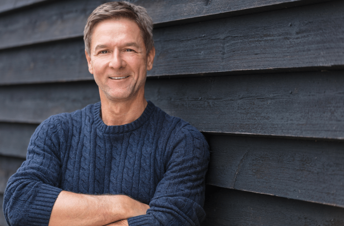 Happy middle aged man leaning on wall with arms crossed