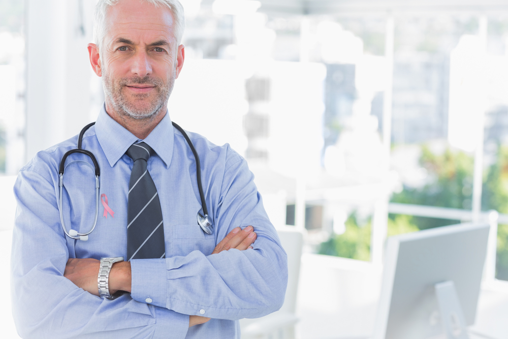 Doctor with arms crossed wearing breast cancer awareness ribbon